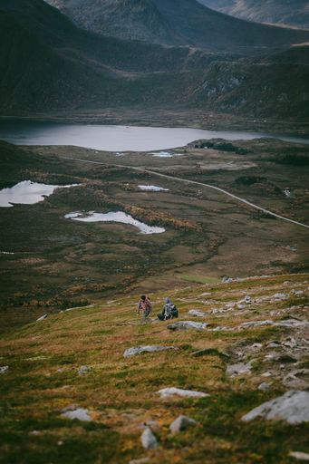 A vertical shot of hikers sitting on a hill with a lake and mountains in background