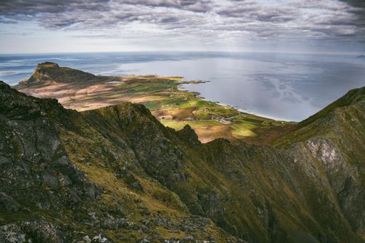 An aerial shot of a rocky mountain and coastal plains under a cloudy sky