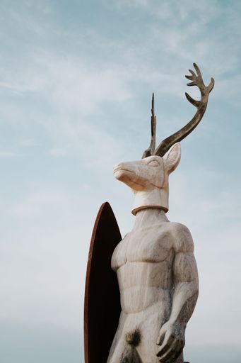 A vertical shot of the Surfer Deer Man sculpture from Nazareth under a blue cloudy sky