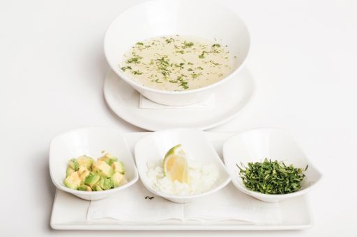 A closeup shot of a delicious soup served with cut avocado, lime and seasoning