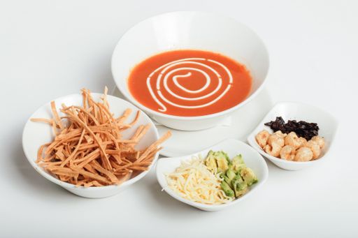 A closeup of a tomato soup with side dishes on a white background