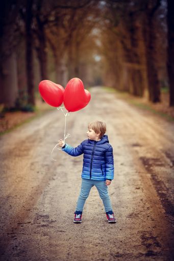 A vertical shot of a child holding heart-shaped balloons while standing on a gravel road