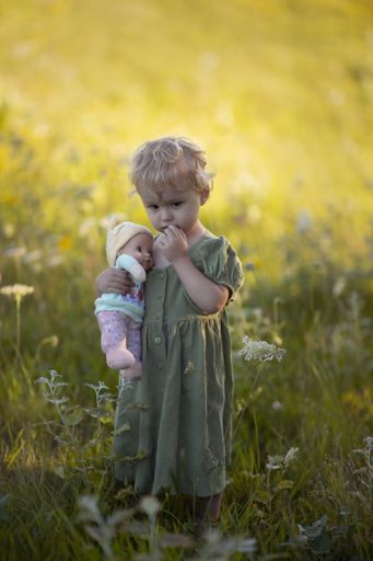 A vertical shot of an adorable child hugging her doll while standing on the grass-covered meadow