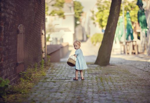 A cute child holding a basket and walking on the pavement by the old houses