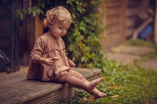 An adorable child eating a cookie while sitting barefoot on the porch