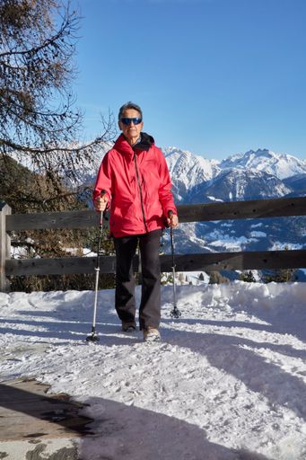 A vertical shot of the hiker leaning on a fence in the Swiss Alps in snowy mountain landscape