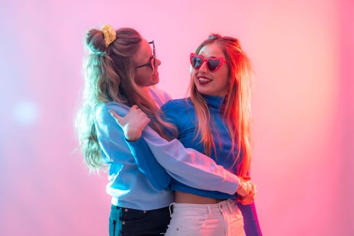 Two females embracing in a warm hug illuminated by bright neon lights creating clubbing atmosphere