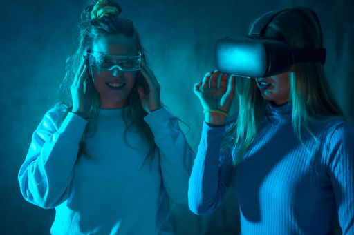 Two females wearing virtual reality glasses in a dimly lit room exploring the virtual reality