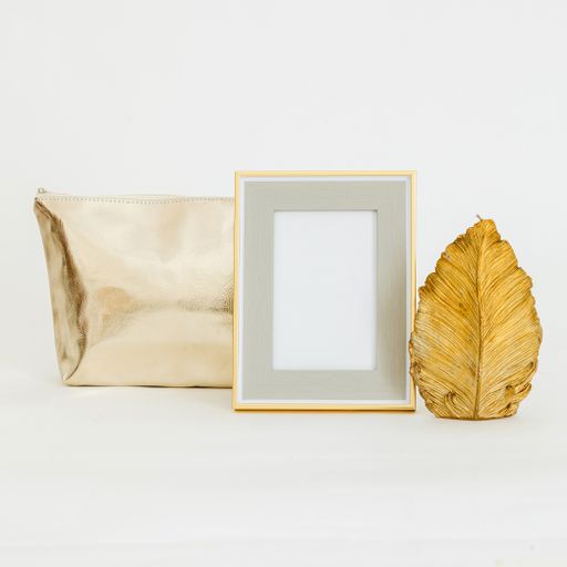 An isolated closeup of anempty golden frame mockup next to a cosmetic bag and golden leaf sculpture