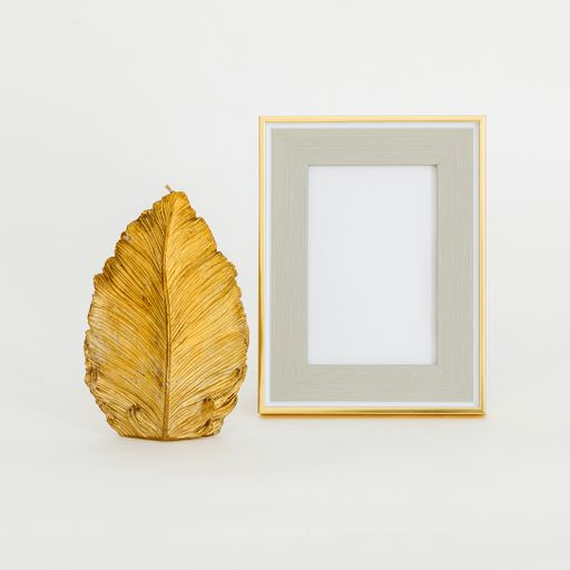 An isolated closeup of an empty golden frame mockup next to a golden leaf sculpture