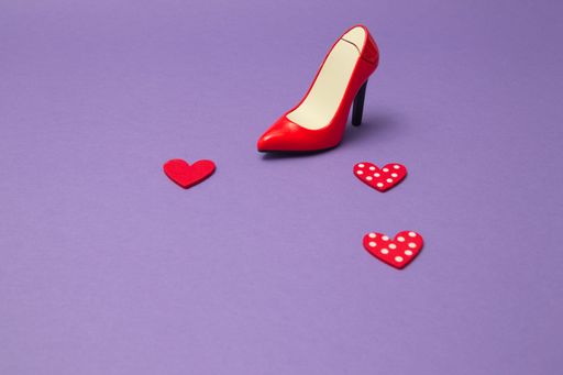 A red female high heels on purple background with red hearts and copy space- the concept of Valentine