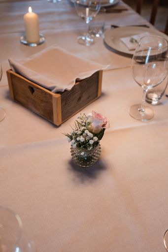 This image depicts a wedding decorations including small glass vase sitting atop a wooden table