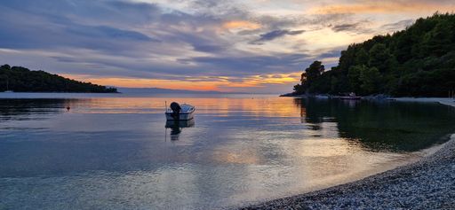 Panormos Beach is illuminated by a warm, golden sunset, with a single boat peacefully standing in the middle of the composition