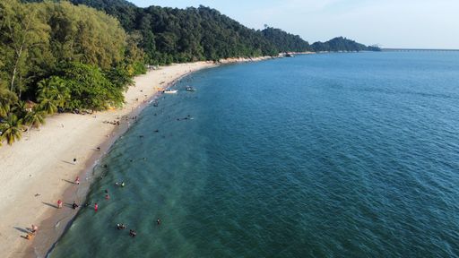 A drone view of the sandy beach with swimming people in the turquoise sea surrounded by green hills and trees in the daytime