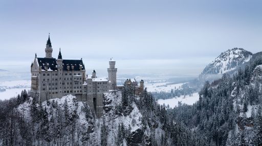 An aerial view of the historic Neuschwanstein castle on a snowy hill in the Alps