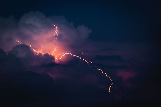 A dramatic sky with illuminated clouds by a lightning strike over a cityscape at night
