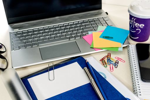 A closeup of a messy desk with a laptop, notepads, and notes on it in the office