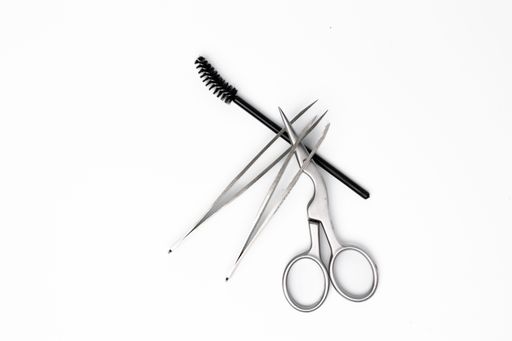 A top view of a stainless steel scissor, two tweezers and spoolie brush isolated on a white background