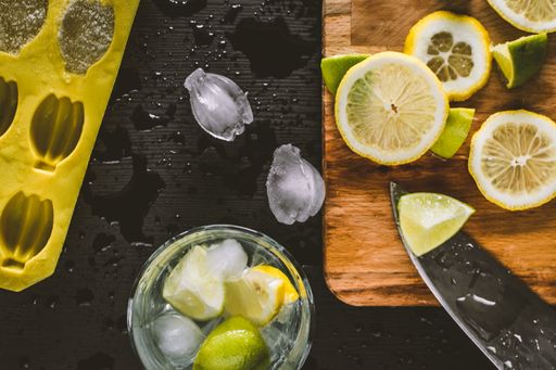 A top view of mojito preparation with sliced lemons, ice cubes, and knife on the counter