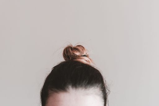 A woman head with cute small bun against light gray wall with copy space