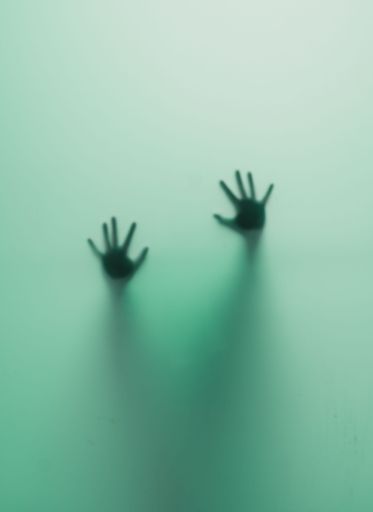 A vertical shot of blurred human hands behind a green glass