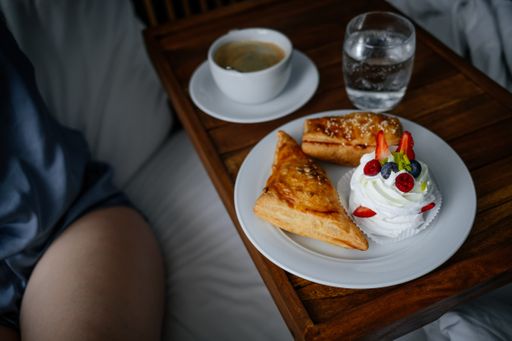 A closeup of a cup of coffee with delicious pastries on a board on the bed