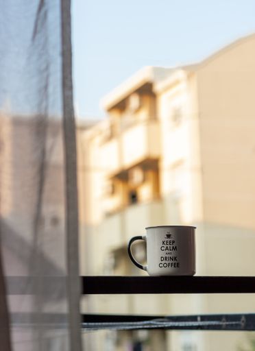 A vertical selective focus of a mug on a window sill with buildings in the background
