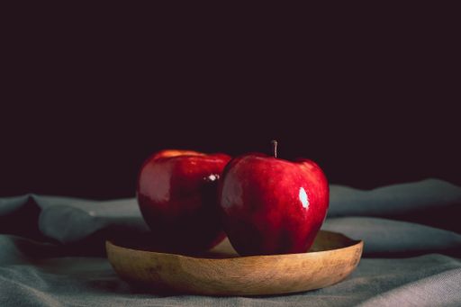 Still life of two red apples on a wooden plate and a gray tablecloth on a black background. Minimalist dark food concept with copy space for text