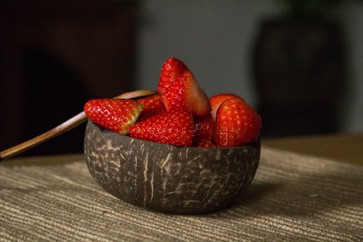 A selective focus shot of fresh strawberries in a bowl with a wooden spoon