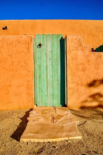 A vertical shot of a bright orange wall with a rustic wooden doorway in Borrego Springs, California