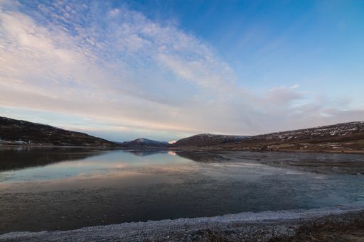 A river surrounded by hills covered in the snow under a cloudy sky during the sunset in Iceland