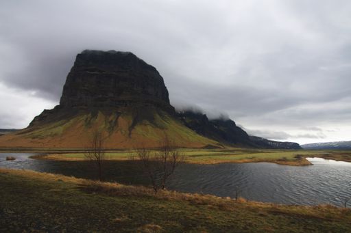 A lake surrounded by rocks covered in greenery and fog under a cloudy sky in Iceland