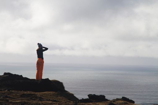 A woman standing on the rock surrounded by the sea under a cloudy sky in Iceland