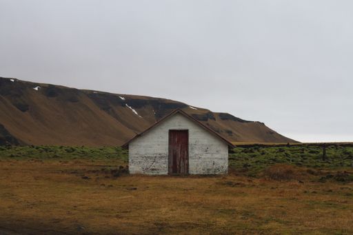 An old barn in a field surrounded by hills under a cloudy sky in Iceland