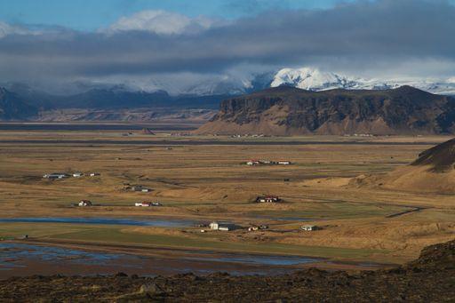 A field surrounded by water and hills covered in the snow under a cloudy sky in Iceland