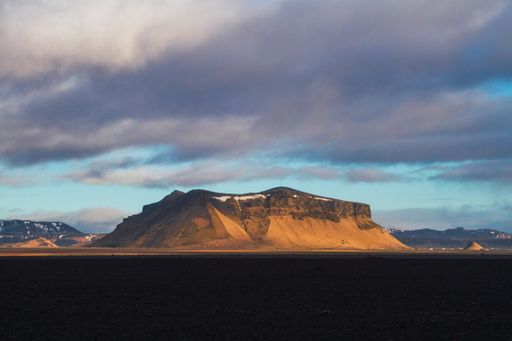 A field surrounded by rocks covered in the snow under a cloudy sky during the sunset in Iceland