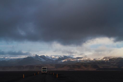 A bus on the road surrounded by rocks covered in the snow under a cloudy sky in Iceland