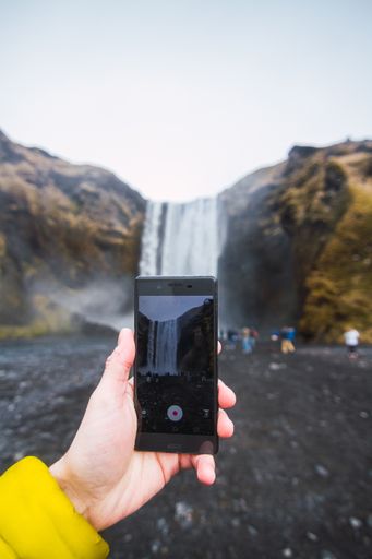 A closeup of a hand taking a video of the Skogafoss waterfall with a phone in Iceland