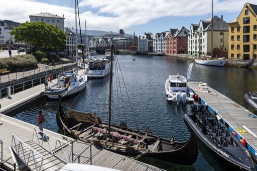 Several boats on a wide water canal surrounded by colorful buildings in Alesund, Norway