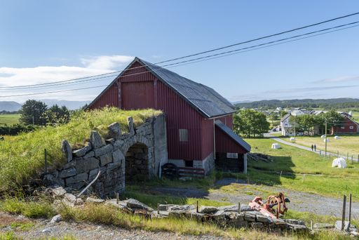 An old stone bridge connecting to a red barn surrounded by greenery and short trees in Alesund, Norway
