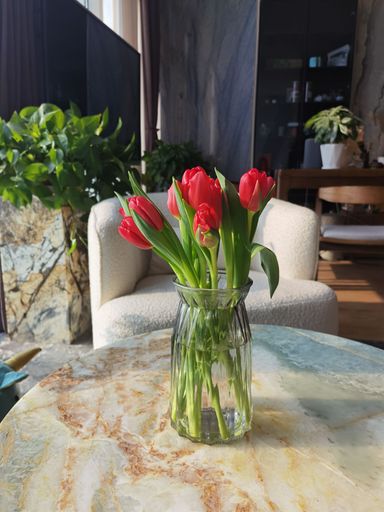 A vertical closeup of a vase with red tulips on a marble table