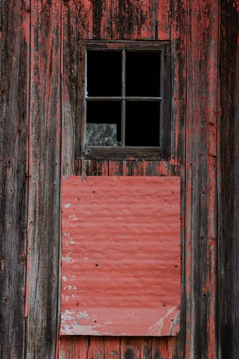 A vertical shot of an old rural wooden red and brown door and a window of a hut