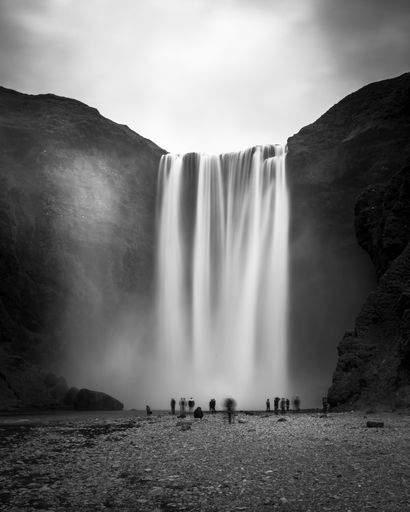the majestic Skogafoss waterfall cascading down a hillside and hikers near the shoreline