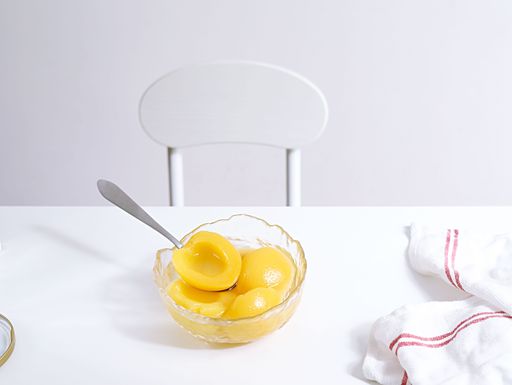 A glass bowl filled with yellow peaches on white background