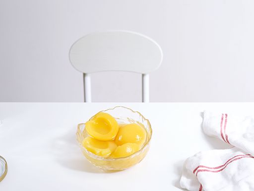 A glass bowl filled with yellow peaches on white background