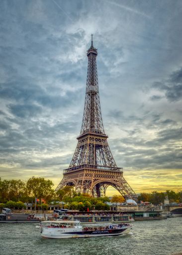 A vessel sailing down the tranquil river with the iconic Eiffel Tower in the background at sunset