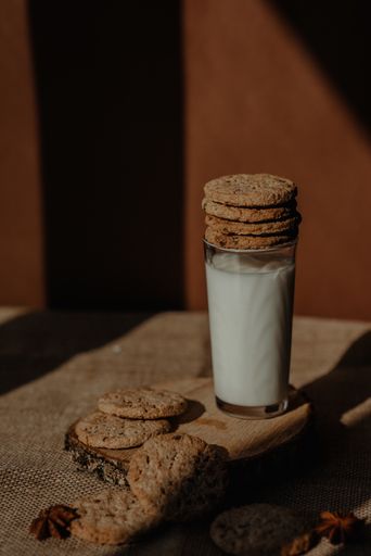 A vertical shot of a glass of fresh milk on a rustiwood coaster with stack of cookies on top