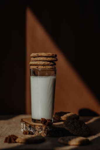 A vertical shot of a glass of fresh milk on a rustic wood coaster with stack of cookies on top