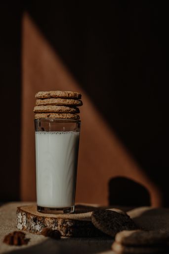 A vertical shot of a glass of fresh milk on a rustic wood coaster with stack of cookies on top