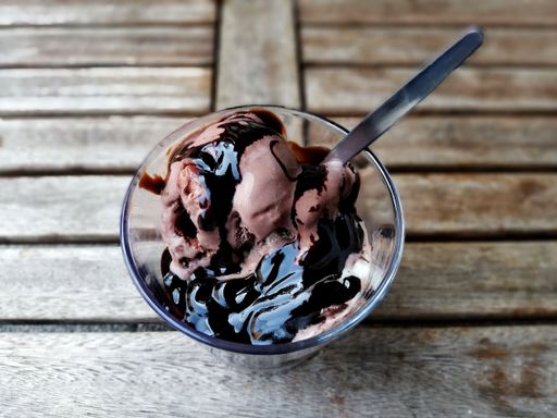 A top view of chocolaty Ice cream in a glass bowl with a spoon isolated on the wooden background